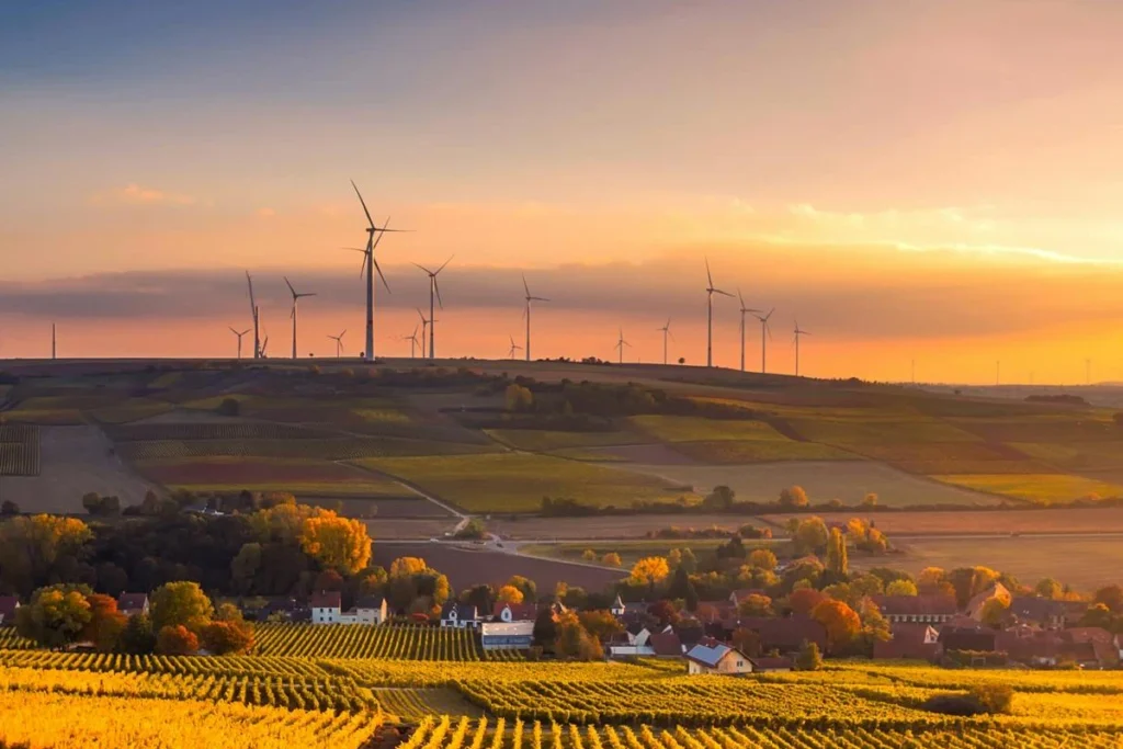 a small town in the country with wind turbines in the background at sunset